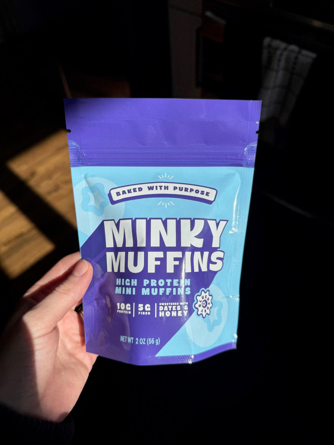 A hand holding an unopened bag of Minky Muffins blueberry mini muffins