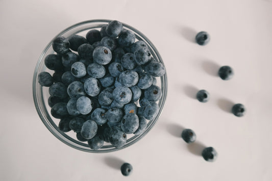 a small glass bowl overflowing with blueberries and a sprinkle of blueberries next to the bowl.