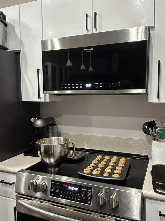 Kitchen oven and stovetop with freshly baked muffins cooling down and a mixing bowl with batter. 